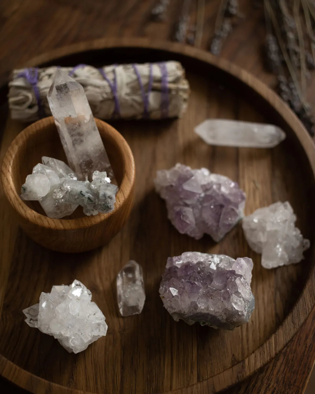 Amethyst clusters, quartz points and white sage on a wooden tray